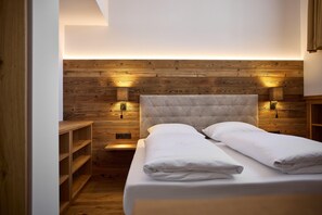 A bedroom with a wooden headboard, two bedside lamps, a bed with white linens, and built-in shelving. - Penthouse Suite With Panoramic Views (Gaschurn)