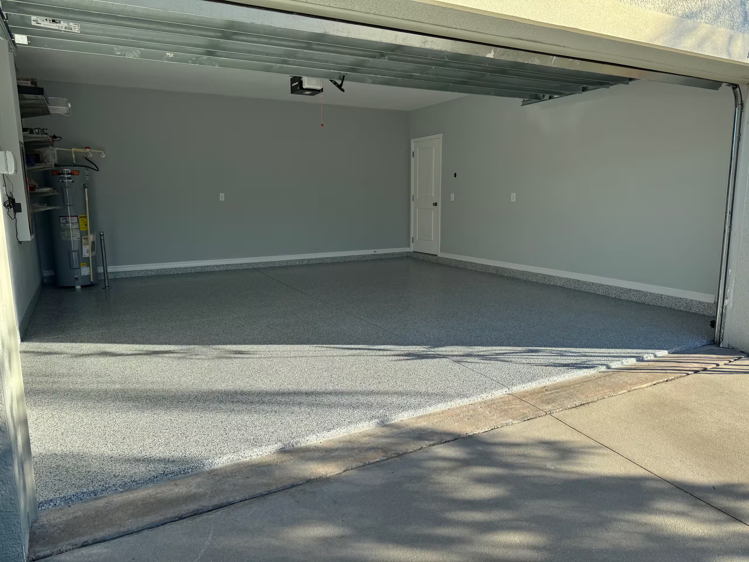 Un garage avec un sol en béton, une porte fermée et un chauffe-eau situé à gauche.