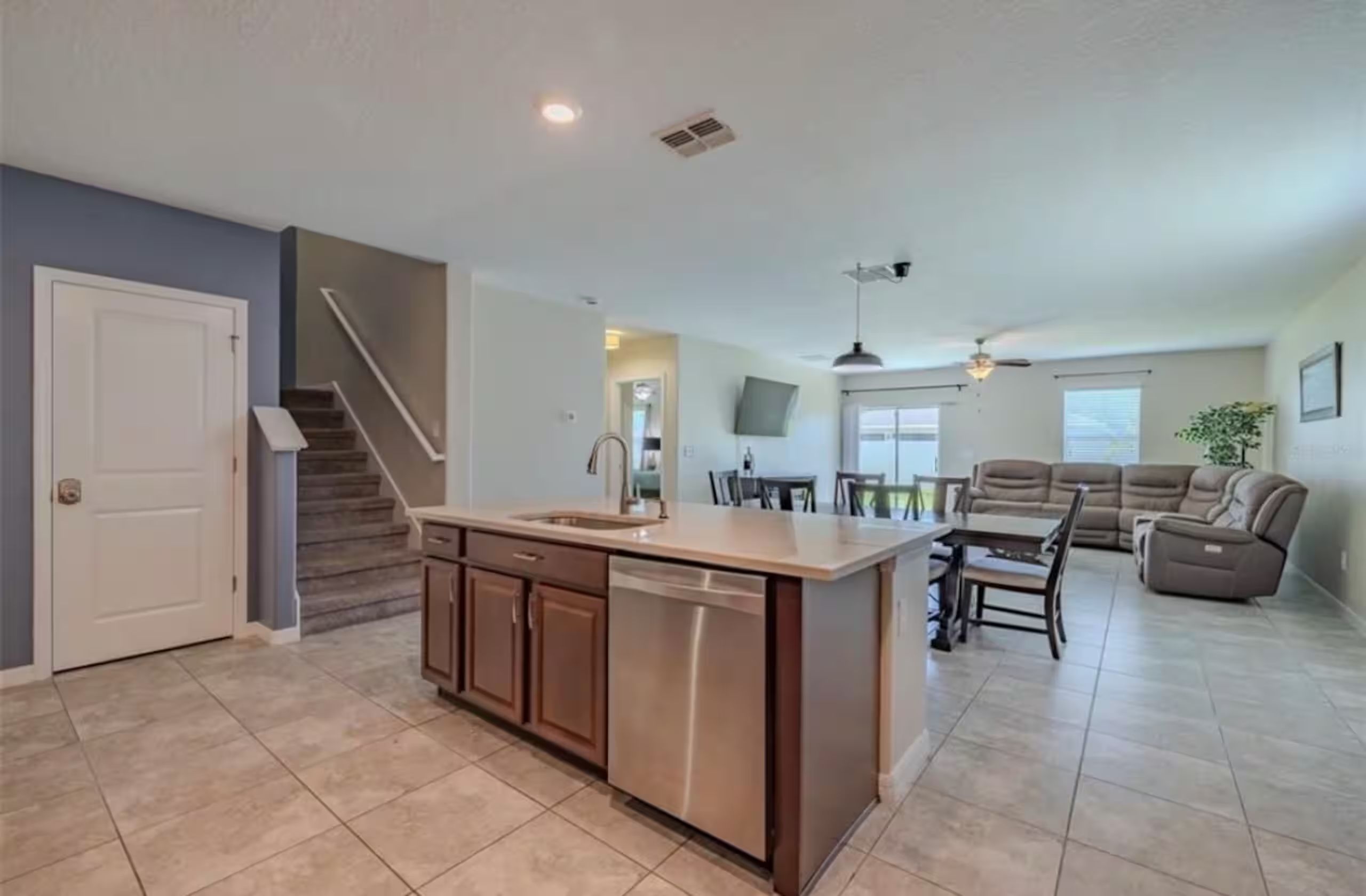 A spacious kitchen with a central island, a dining area with a sofa and chairs, and a staircase leading to another level.
