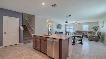 A spacious kitchen with a central island, a dining area with a sofa and chairs, and a staircase leading to another level.