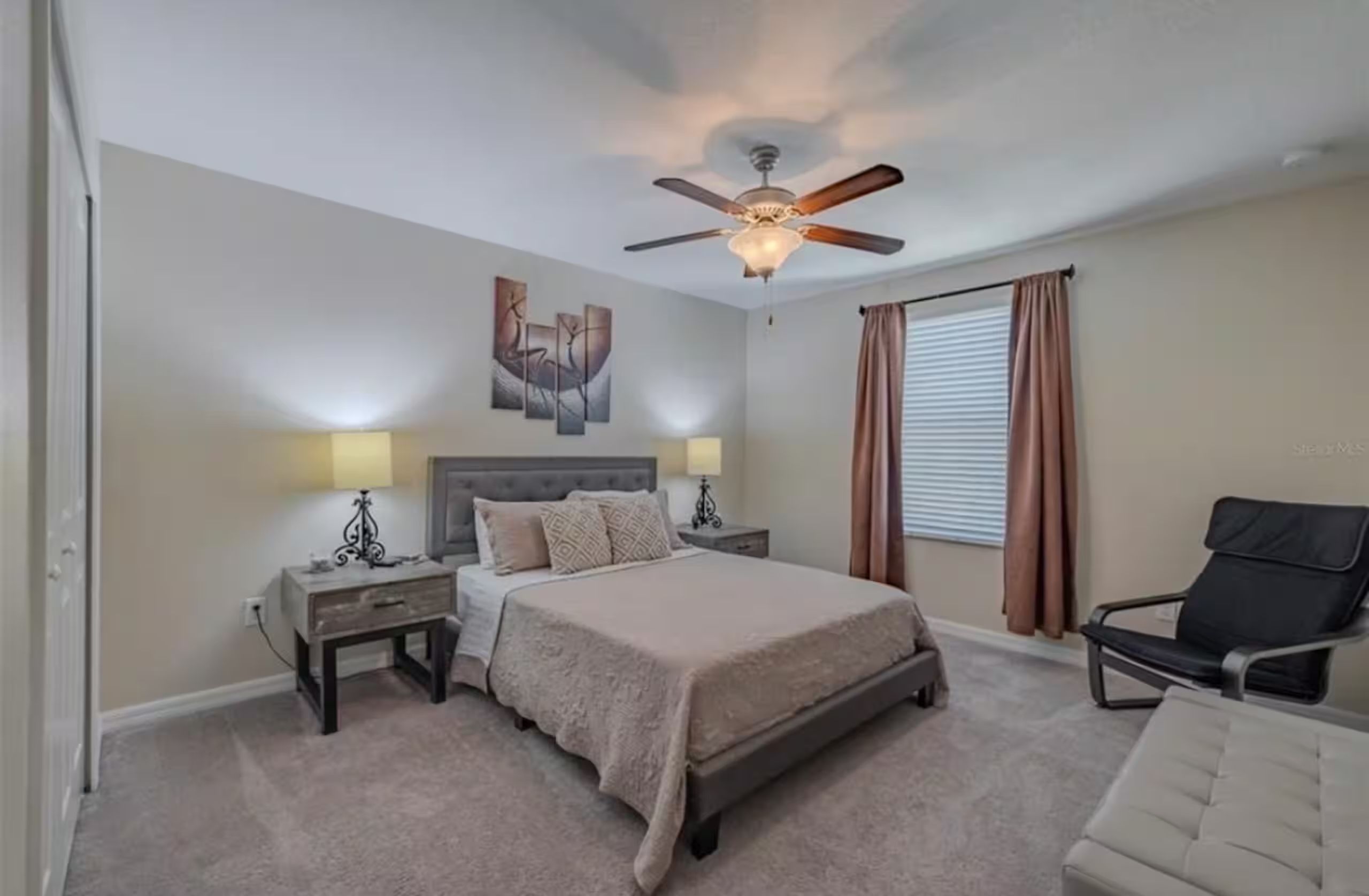 A bedroom with a bed, two bedside tables, a ceiling fan, a window with curtains, and a chair.