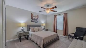 A bedroom with a bed, two bedside tables, a ceiling fan, a window with curtains, and a chair.