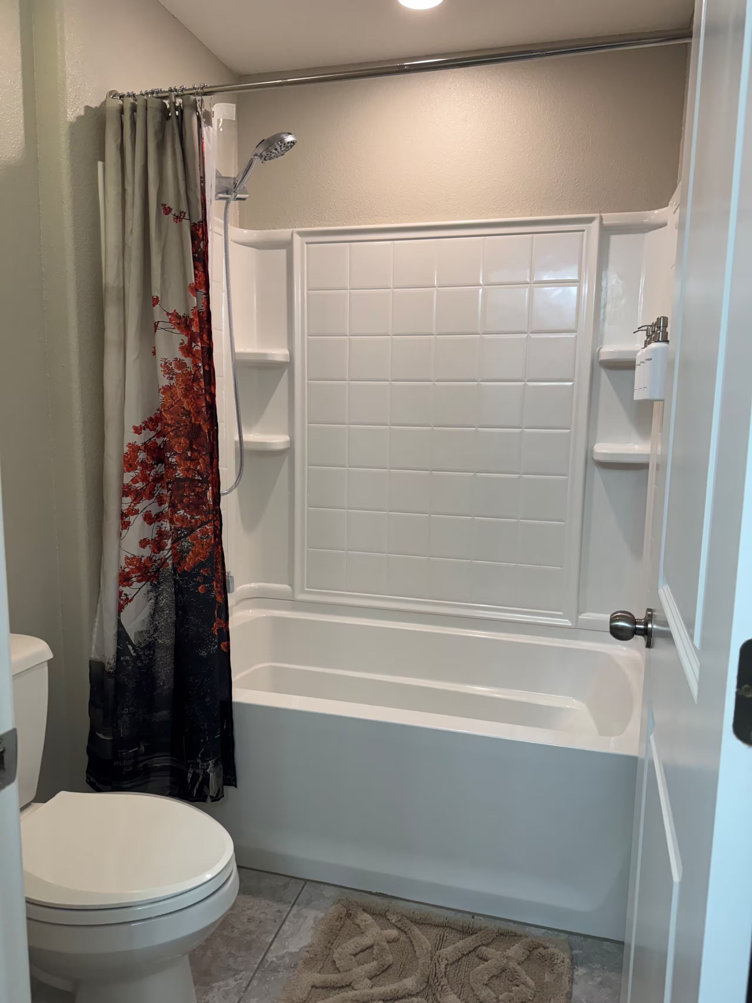 A bathroom with a white bathtub, a shower, a toilet, and a patterned shower curtain.