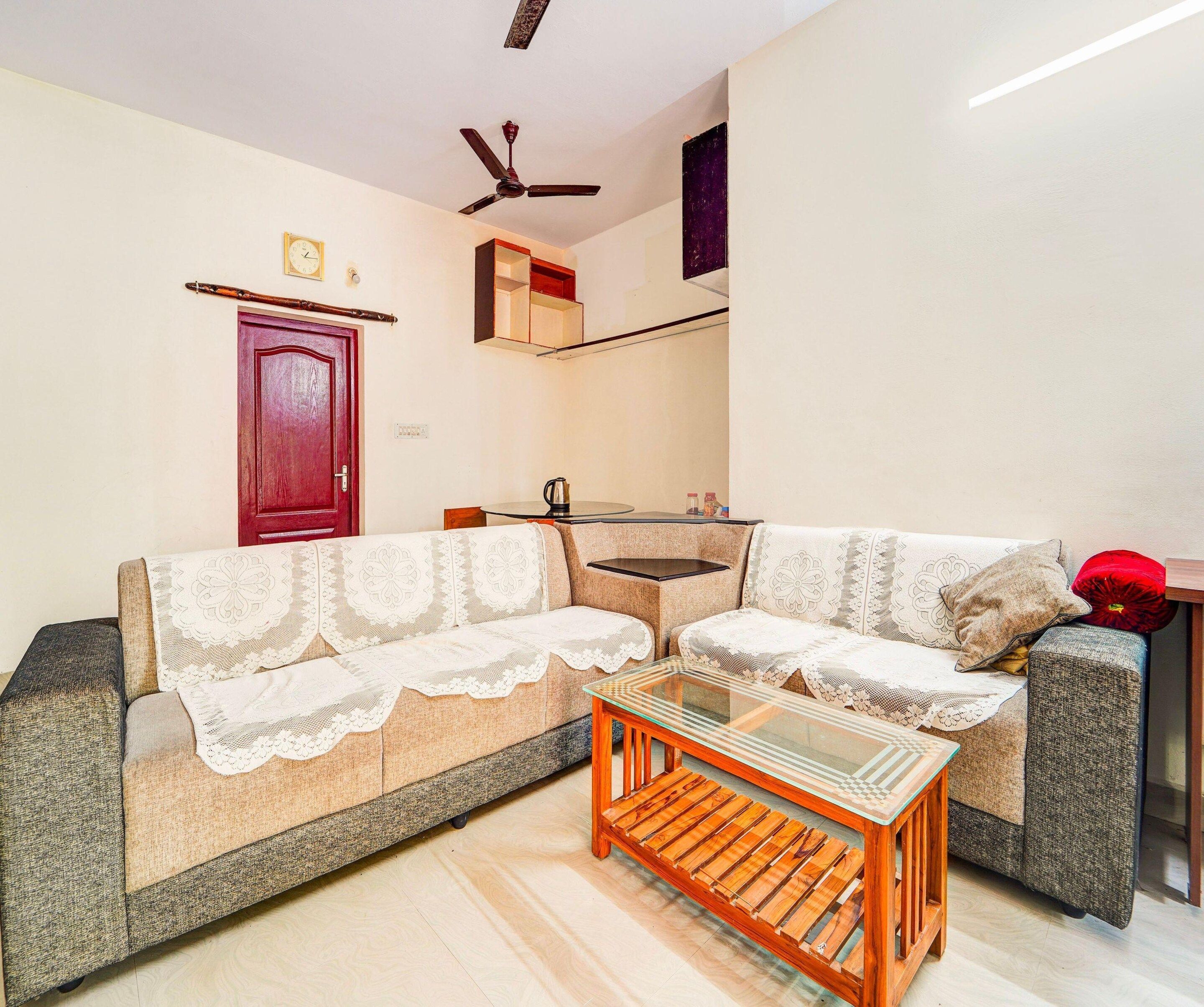 A living room with a sofa, a coffee table, a ceiling fan, and a door.
