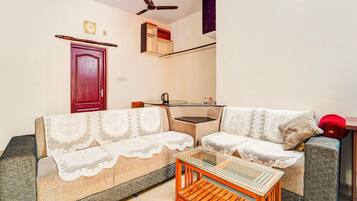 A living room with a sofa, a coffee table, a ceiling fan, and a door.