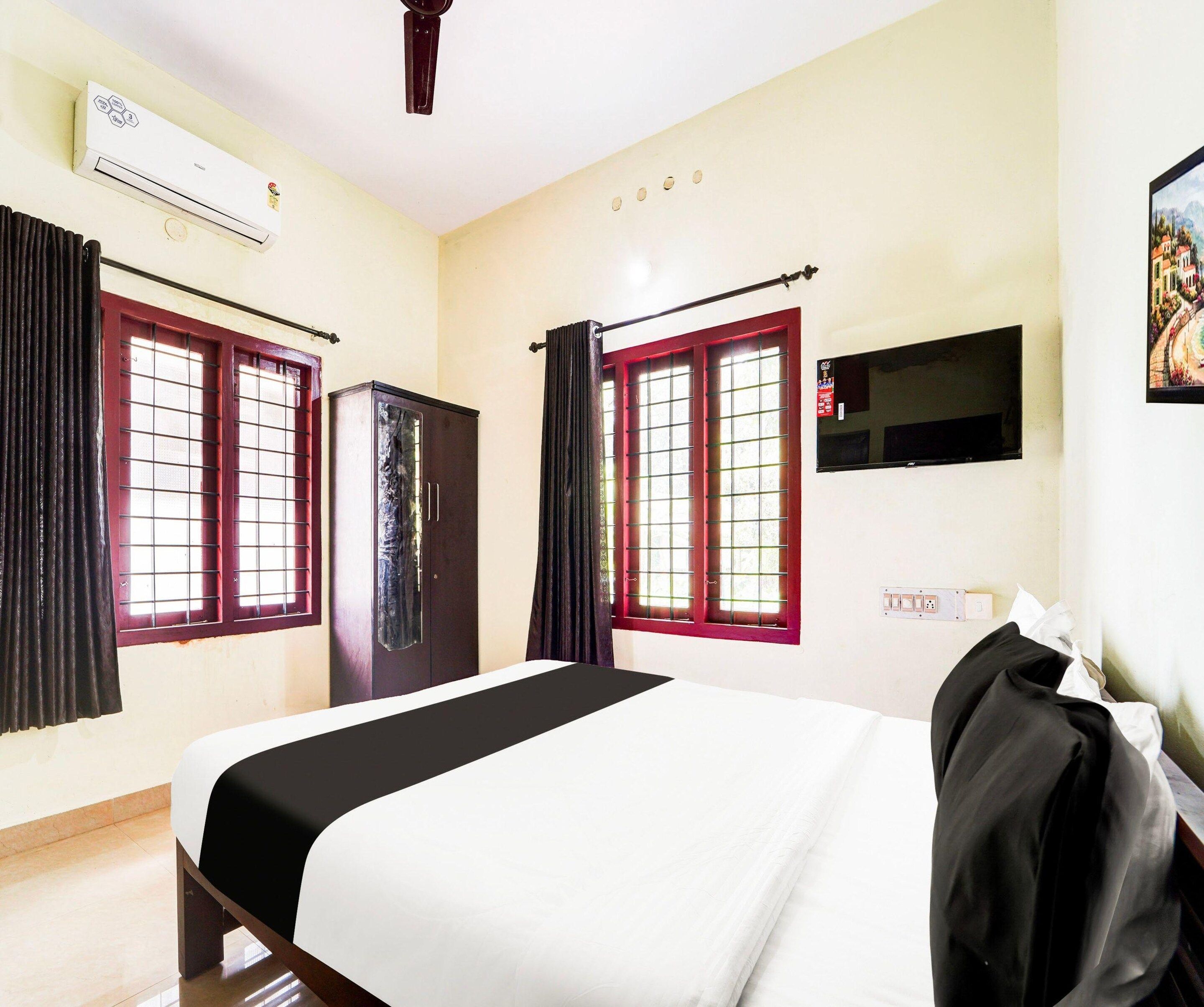 A hotel room with a bed, a wardrobe, a TV mounted on the wall, and a window with curtains.