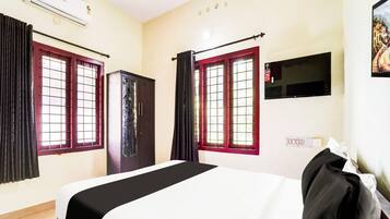 A hotel room with a bed, a wardrobe, a TV mounted on the wall, and a window with curtains.