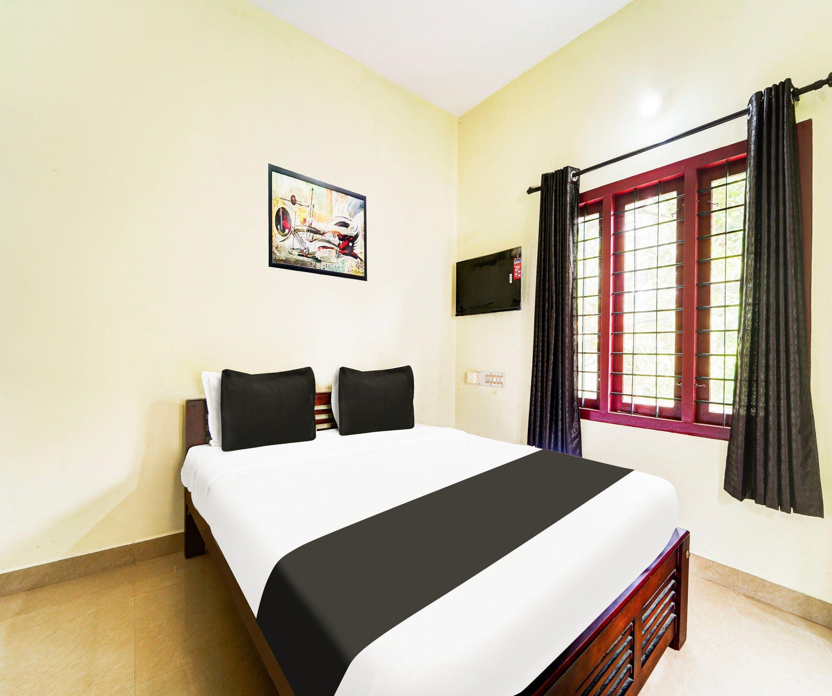 Habitación de hotel con cama, un cuadro en la pared, ventana con cortinas y televisor de pared.