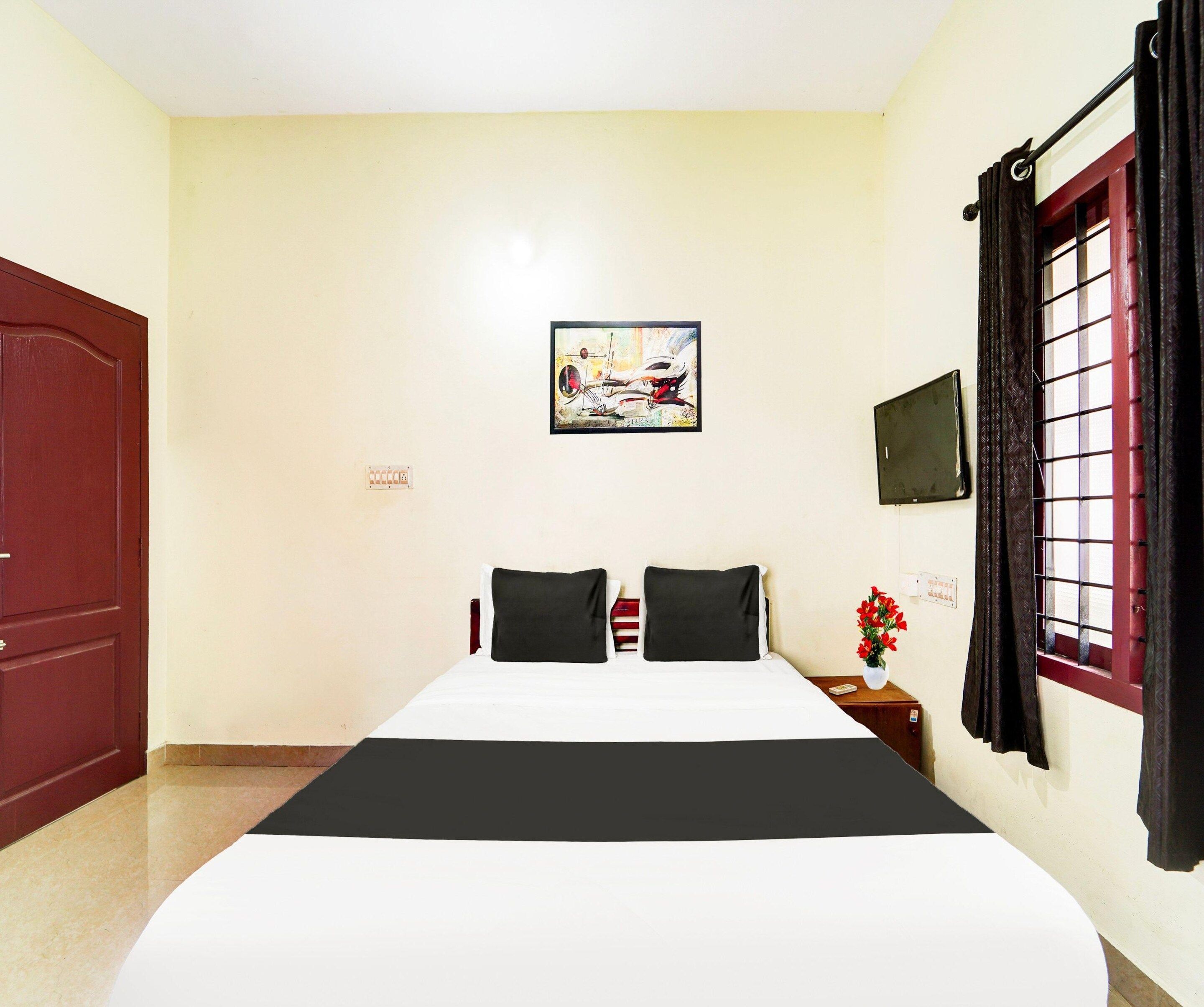 A hotel room with a bed, a painting, a TV, a window with curtains, and a door.
