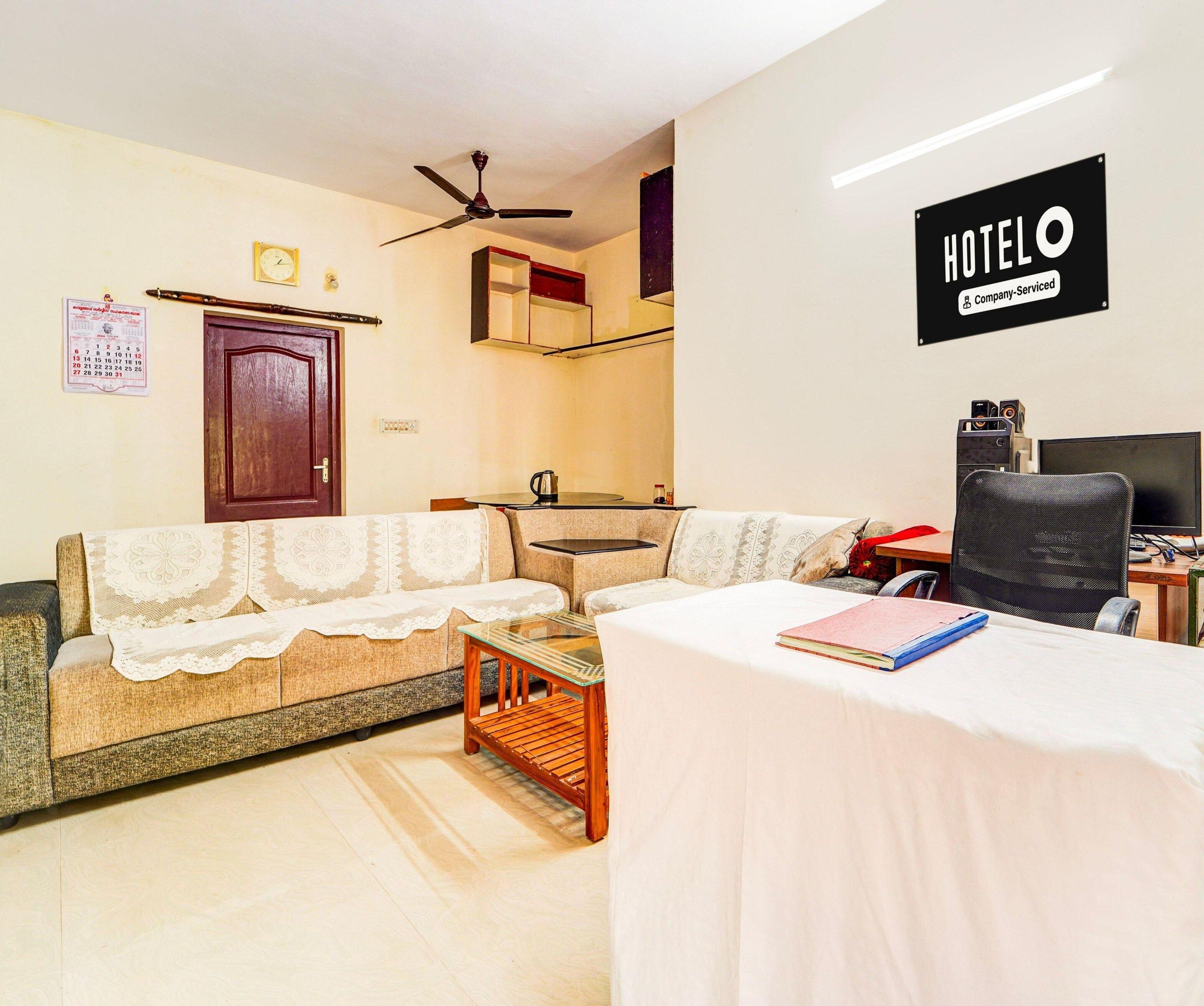 A hotel room with a sofa, a small table, a bed, a desk with a computer, and a ceiling fan.
