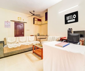 Habitación de hotel con sofá, una pequeña mesa, cama, escritorio con computadora y ventilador de techo.