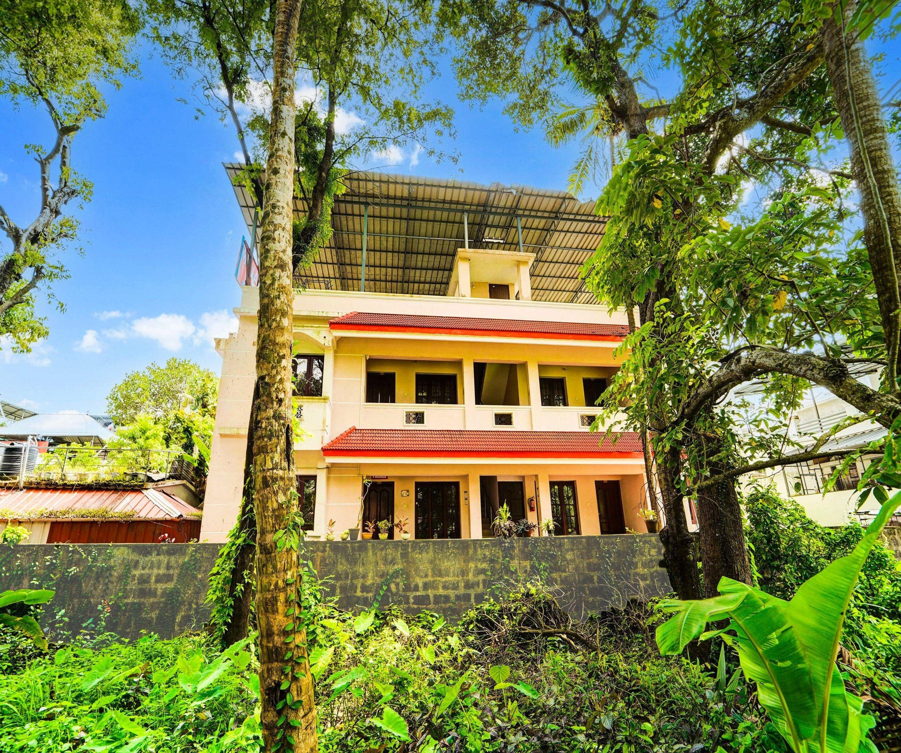 A multi-story building with a red roof, surrounded by lush greenery and trees.