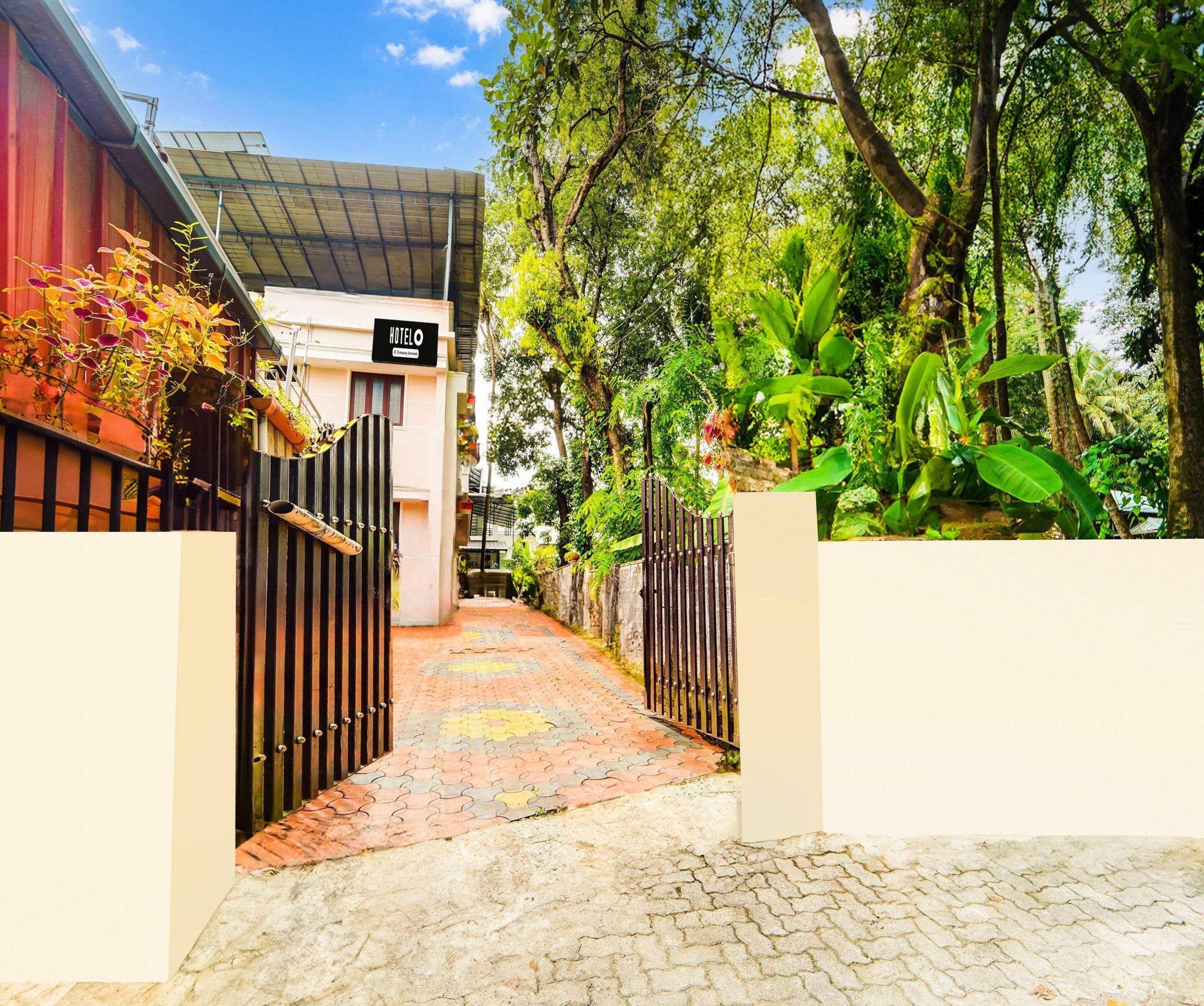 A hotel entrance with a paved pathway leading to a gated entrance, surrounded by lush greenery and trees.