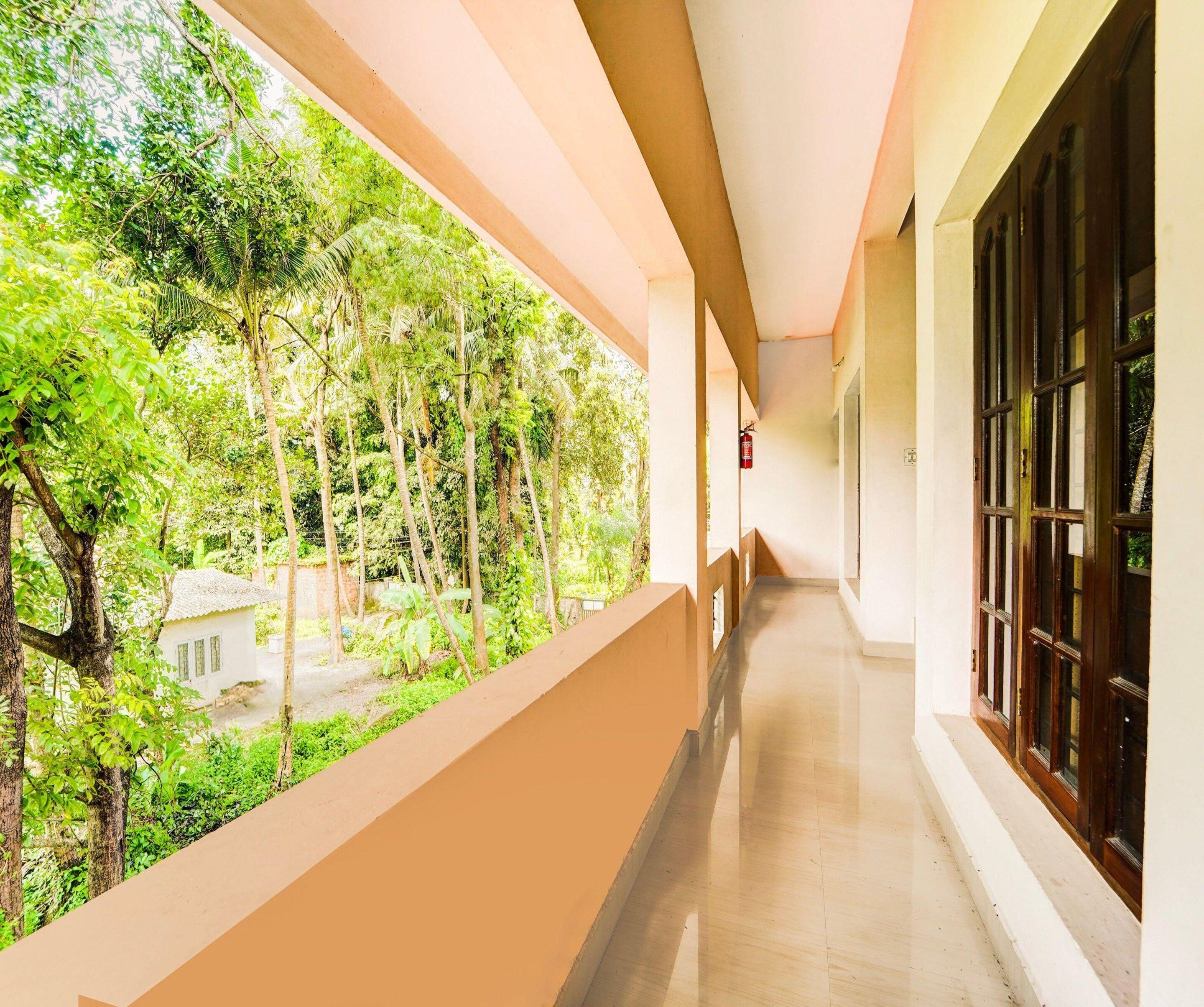 A corridor with a view of a lush garden and a building with large windows.