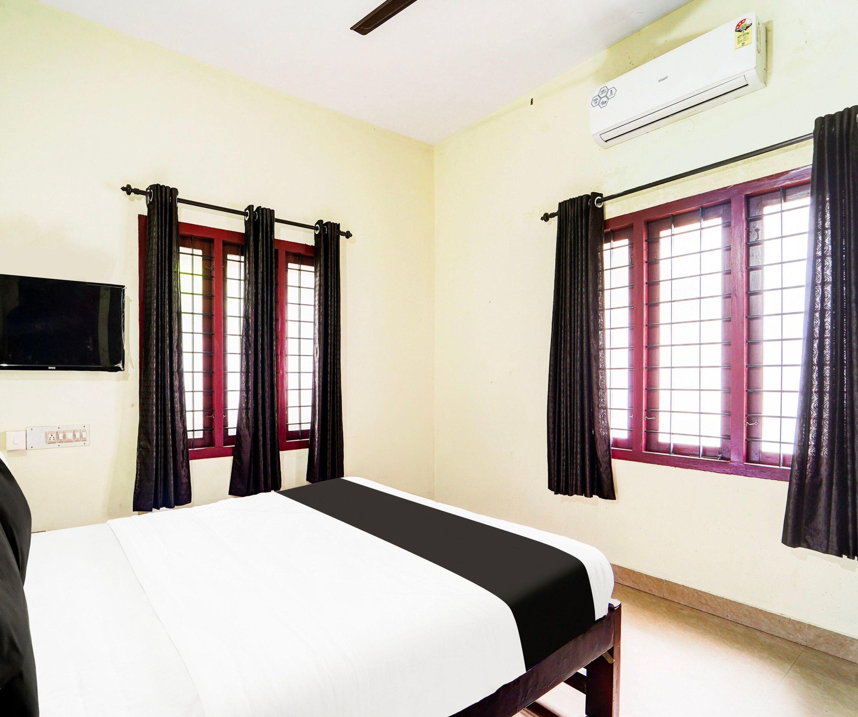 Une chambre avec un lit, deux fenêtres avec des rideaux, un appareil de climatisation et un téléviseur fixé au mur.