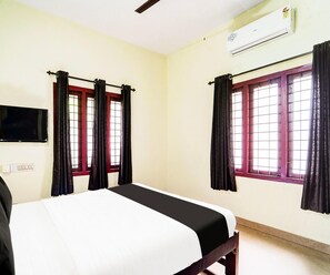 A room with a bed, two windows with curtains, an air conditioning unit, and a television mounted on the wall.