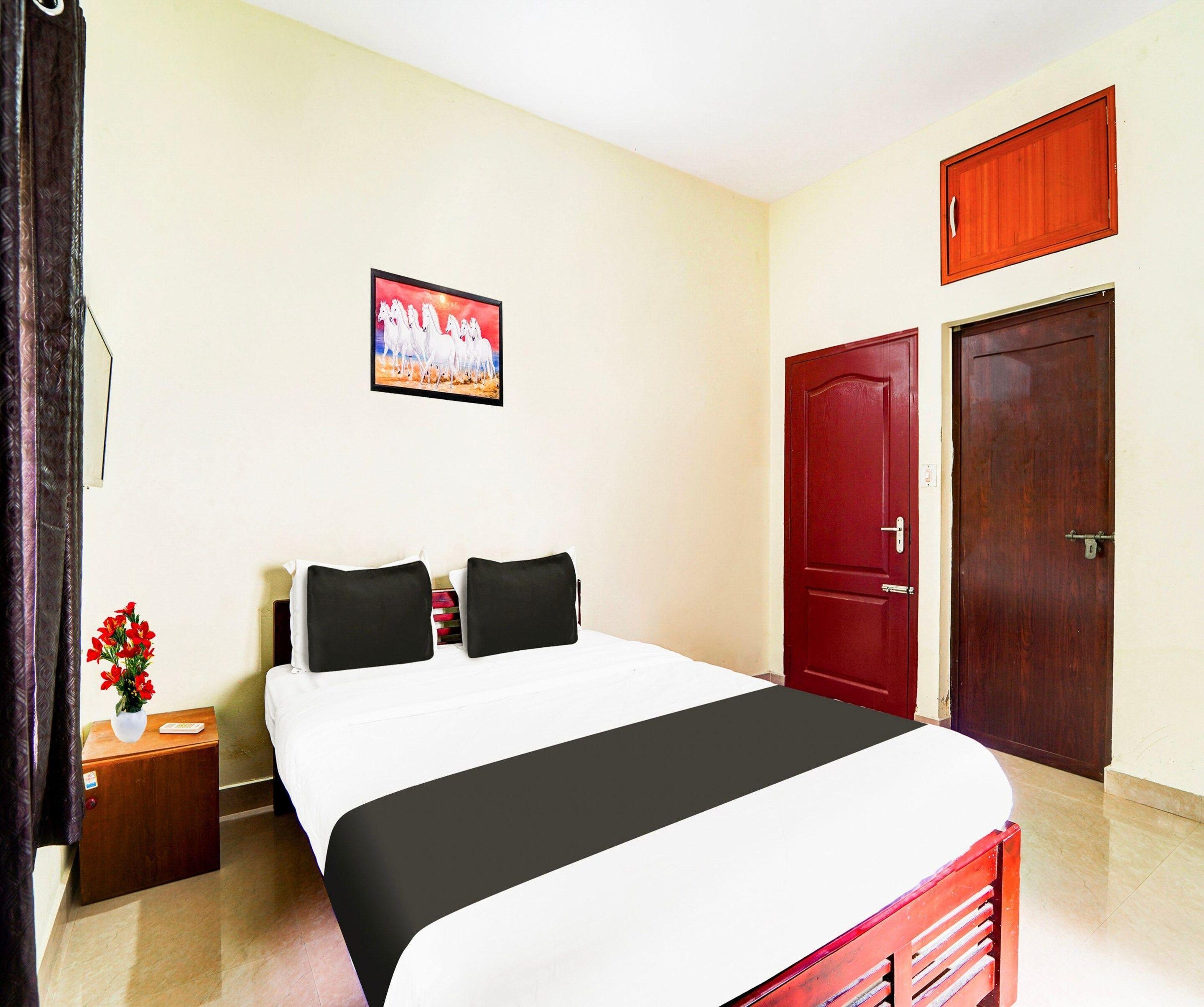 Habitación de hotel con cama, mesita de noche, un jarrón de flores, un cuadro y dos puertas.