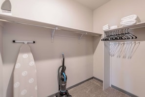 A hotel room with a vacuum cleaner, ironing board, and a closet with hangers and folded towels. - 3BR 2.5BA Modern Farmhouse • King Bed • Smart TVs A (El Paso)
