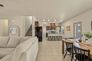 A modern living room with a sofa, a dining area with a wooden table and chairs, and a kitchen with wooden cabinets and a microwave. - 3BR 2.5BA Modern Farmhouse • King Bed • Smart TVs A (El Paso)