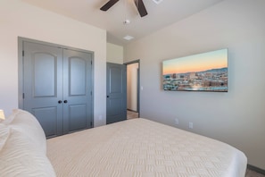A bedroom with a bed, a cityscape painting, and a door leading to another room.