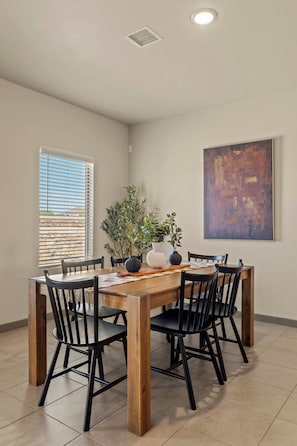 A dining area with a wooden table, black chairs, a potted plant, and a large abstract painting on the wall.