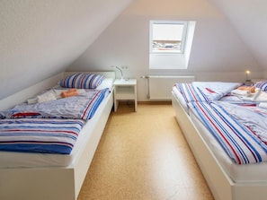 A small, triangular attic bedroom with two beds, a desk, and a window. - Holiday Home With 1 Bedroom (Neuharlingersiel)