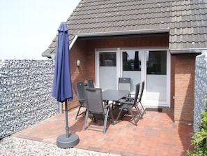 A patio with a table and chairs, a covered umbrella, and a brick wall. - Holiday Home With 1 Bedroom (Neuharlingersiel)
