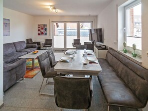 A modern living room with a dining area, grey sofas, a coffee table, and a TV. - Holiday Home With 1 Bedroom (Neuharlingersiel)