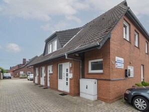 A row of brick buildings with a flat roof, a sign indicating a business, and a car parked in front. - Holiday Home With 1 Bedroom (Neuharlingersiel)