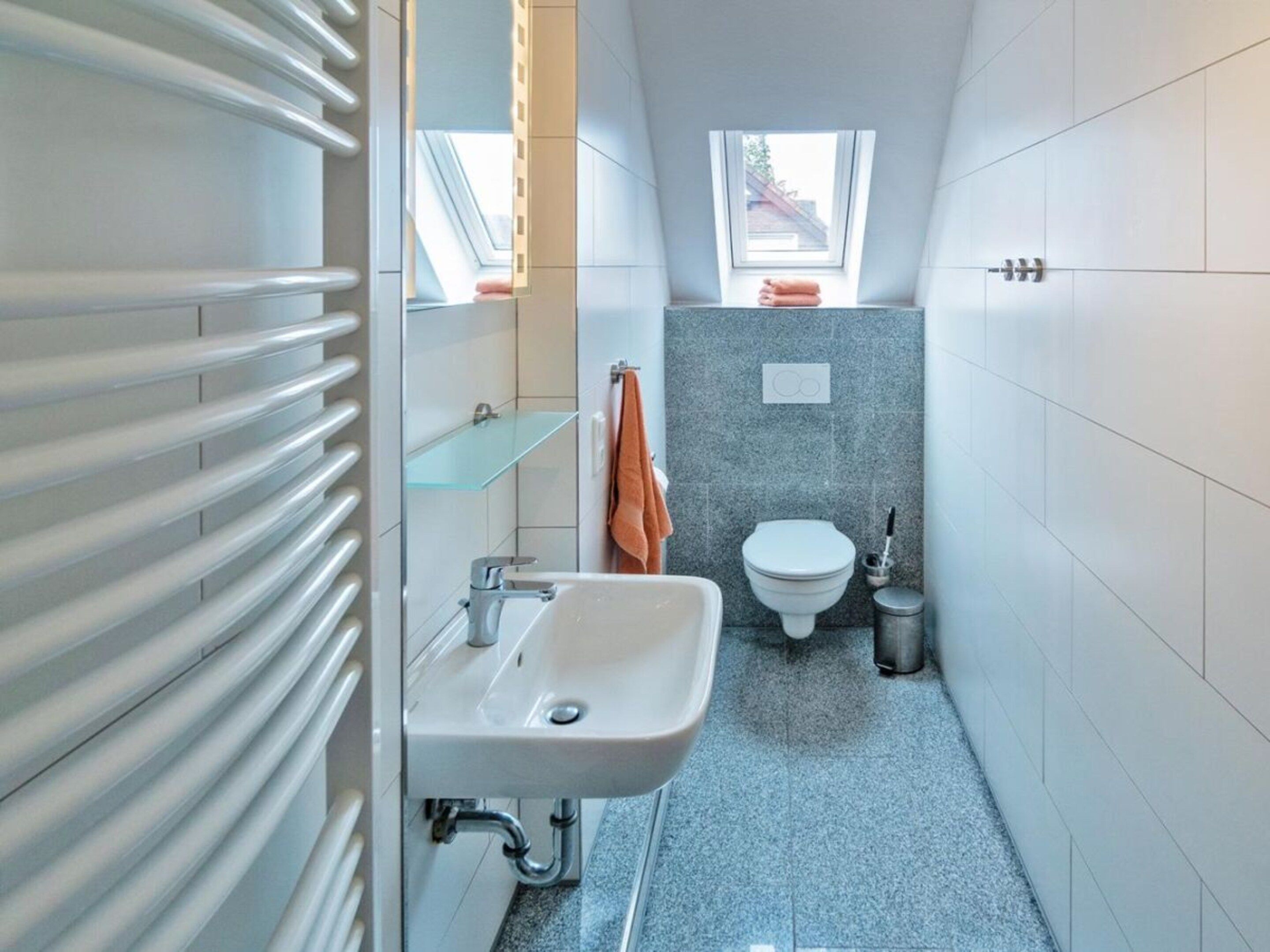 Une petite salle de bain avec un lavabo blanc, des toilettes et une étagère en verre.