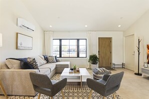 A modern living room with a sofa, two armchairs, a coffee table, and a large window with curtains.