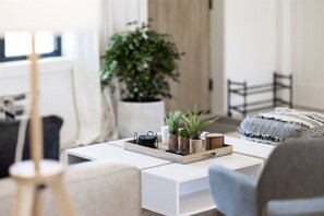A modern living room with a white sofa, a coffee table with decorative items, a potted plant, and a view of the outdoors.