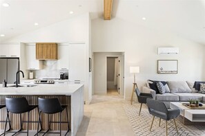 A modern kitchen with a central island, bar stools, and a dining area with a sofa and coffee table.