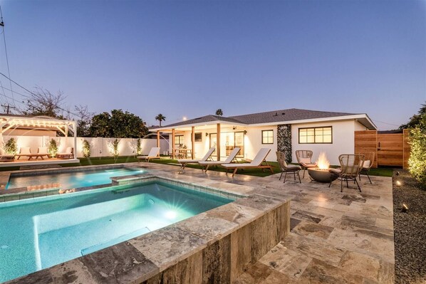 A residential backyard with a swimming pool, lounge chairs, and a fire pit.