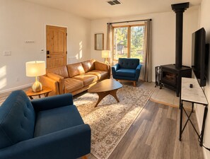 Ein Wohnzimmer mit einer Couch, einem blauen Sessel, einem Couchtisch, einem Kamin und einem Fernseher.