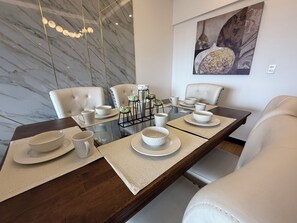 A dining area with a marble wall, a glass table, white chairs, and a painting on the wall.