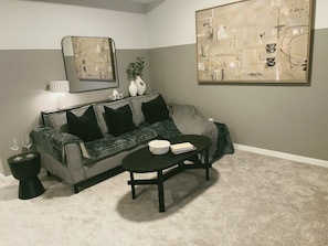 Ein Wohnzimmer mit einem grauen Sofa, schwarzen Kissen, einem schwarzen Couchtisch und einem Bild an der Wand.