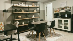 A dining area with a table and chairs, a bookshelf, and a kitchen area with cabinets and appliances. - Modern New 2BR beside Park, 14m WEM, 4m Grocery (Edmonton)