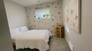 A bedroom with a bed, a window, a wall with a polka dot pattern, and a small wooden cabinet. - Modern New 2BR beside Park, 14m WEM, 4m Grocery (Edmonton)