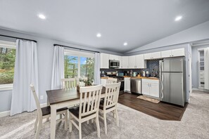 A modern kitchen with white cabinets, stainless steel appliances, and a dining area with a wooden table and chairs.
