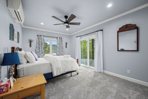 A bedroom with a bed, a ceiling fan, a window with curtains, a bedside table, and a mirror on the wall.