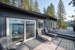 Moderni rakennus, jossa on suuret, liukuvat lasiovet, ulkotila istuimineen ja näköala puilla ympäröidylle järvelle.