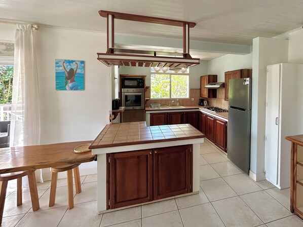 A kitchen with a central island, wooden cabinets, a stainless steel refrigerator, and a window providing natural light.