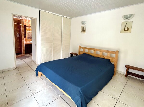 A bedroom with a bed, a wooden headboard, a nightstand, a wardrobe, and a bathroom visible through an open door.