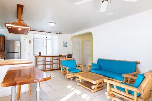 A modern kitchen with a built-in refrigerator, wooden dining table, and a blue sofa with a bamboo frame.