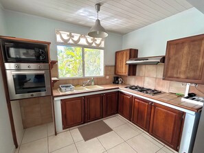 A kitchen with wooden cabinets, a double oven, a gas stove, and a window with a view of greenery.