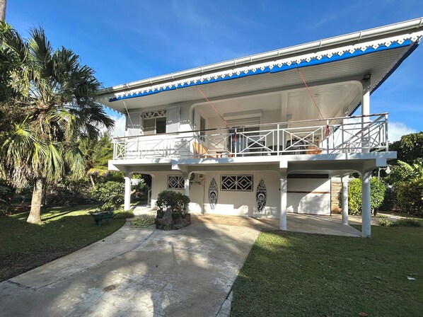 A two-story house with a balcony, a stone sculpture, and a well-maintained lawn.