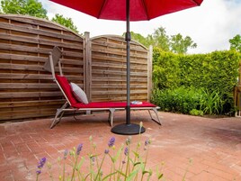 En rød loungeseng med pude, et rundt bord og en rød parasol i en have.