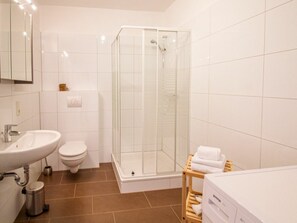Ein modernes Badezimmer mit einer gläsernen Duschkabine, einem Waschbecken, einer Toilette und einem Holzboden mit Handtüchern.