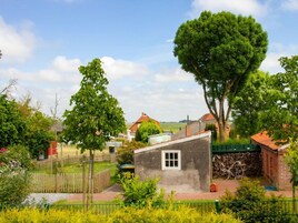 Entorno rural con una casa pequeña, un patio cercado y un árbol grande.